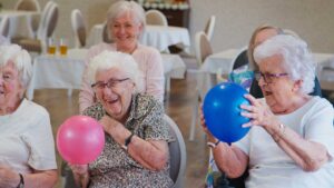 Older adults and staff having a respectful conversation at a communal table in an assisted living residence.