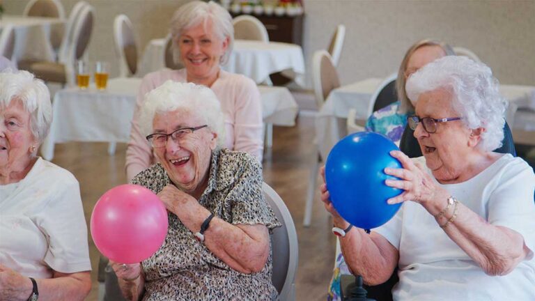 Older adults and staff having a respectful conversation at a communal table in an assisted living residence.